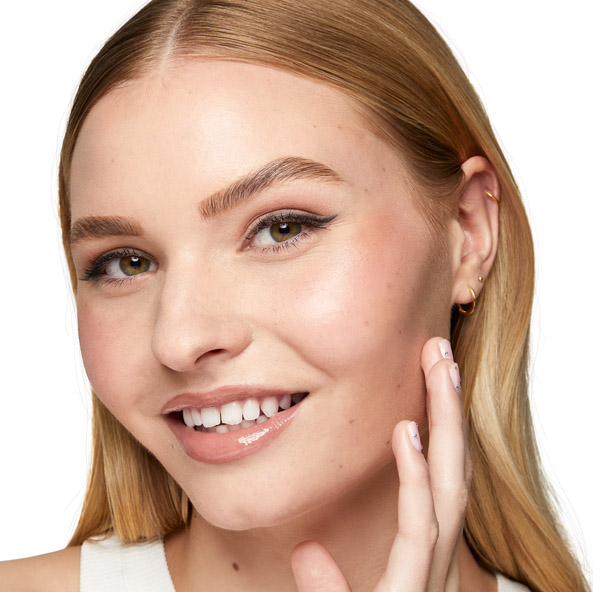 Close-up of a smiling model wearing bronzer and holding a hand up to her face